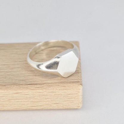 Sterling silver hexagon signet ring side angle on wood, showing tapered shoulders and satin face