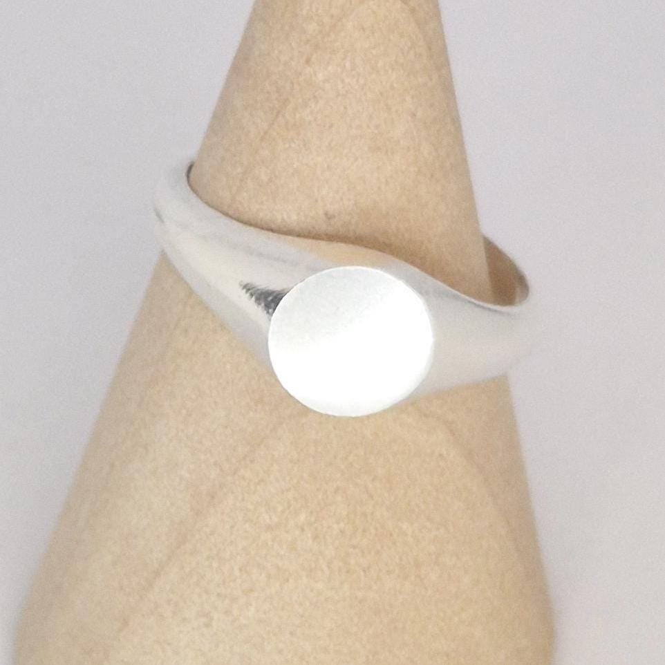 Close-up of signet ring on cone stand, flat circular top detail, polished silver band