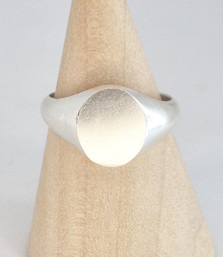 Close-up detail of a handcrafted oval signet ring in sterling or Argentium silver with satin oval face and polished edges.