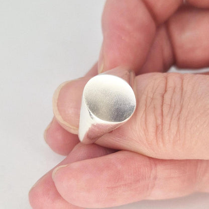 Close-up of a modern oval signet ring in sterling silver showing the brushed oval top and highly polished curved shank.