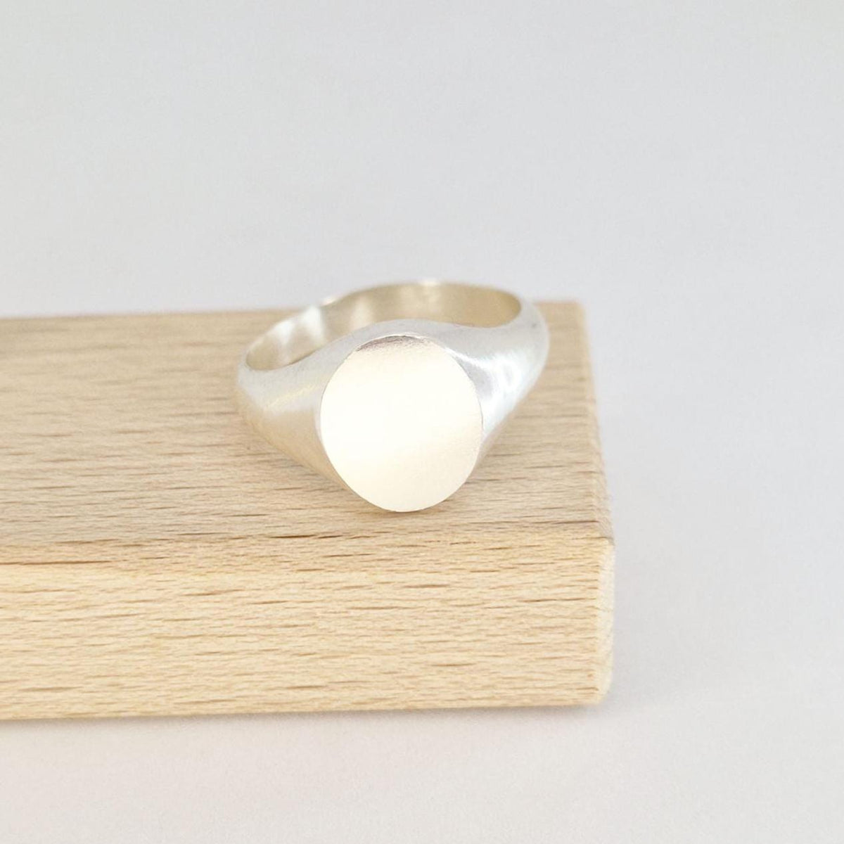 Front view of an oval signet ring in sterling or Argentium silver displayed on a wooden jewellery block with satin-finished face.