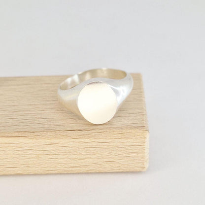 Front view of an oval signet ring in sterling or Argentium silver displayed on a wooden jewellery block with satin-finished face.