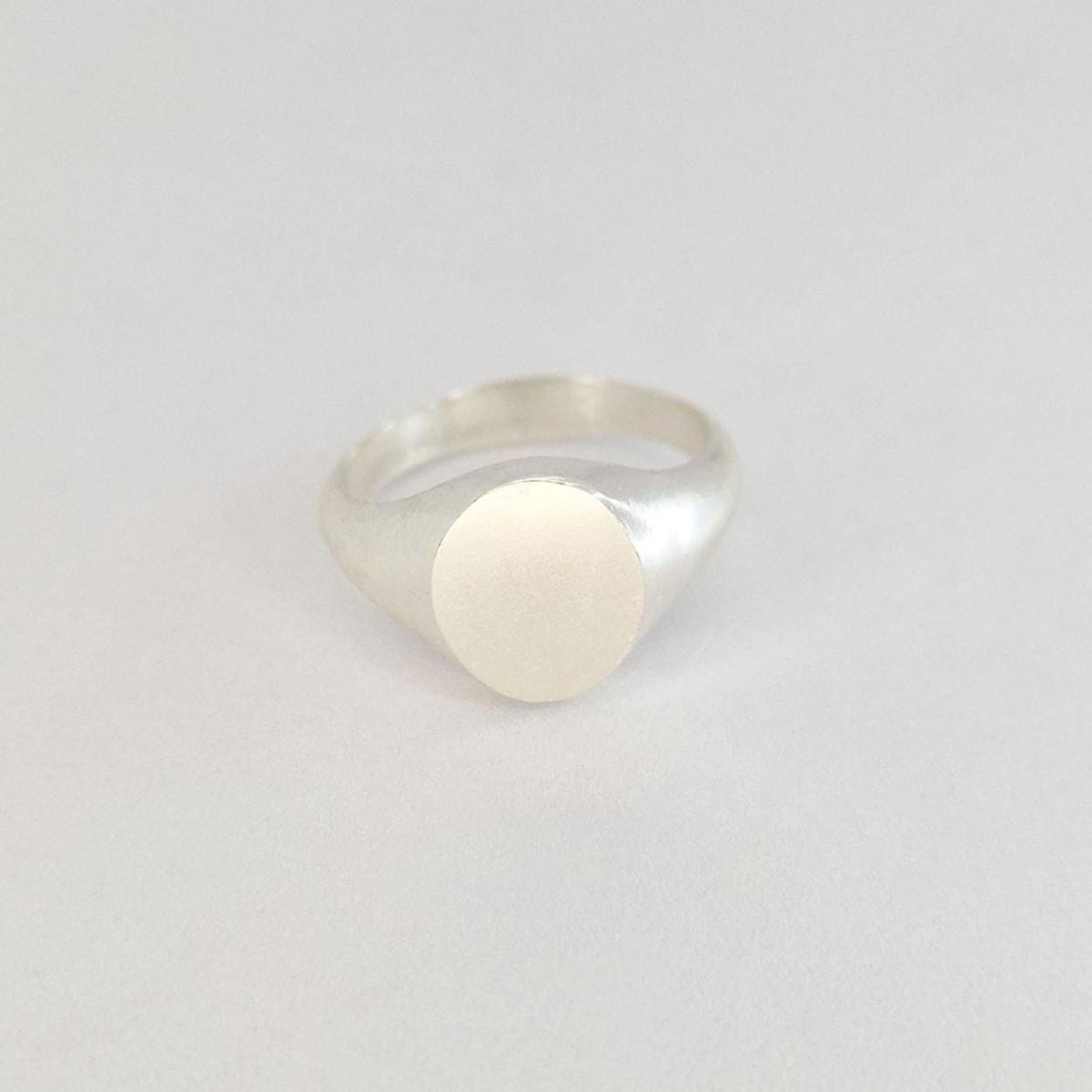 Contemporary oval signet ring with brushed oval face and polished silver band photographed on a soft white background.