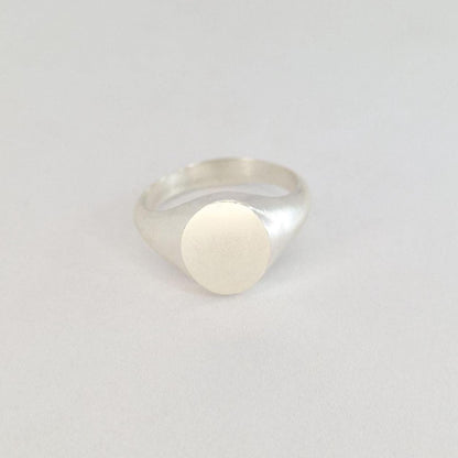 Contemporary oval signet ring with brushed oval face and polished silver band photographed on a soft white background.