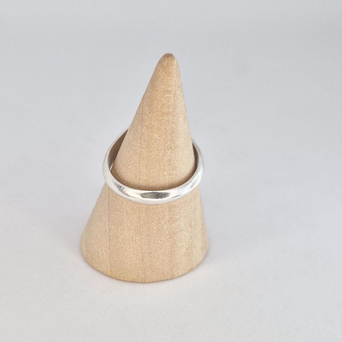 Simple oval signet ring displayed on a wooden cone ring holder, featuring a polished band and satin oval face.