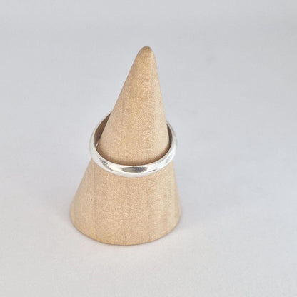 Simple oval signet ring displayed on a wooden cone ring holder, featuring a polished band and satin oval face.