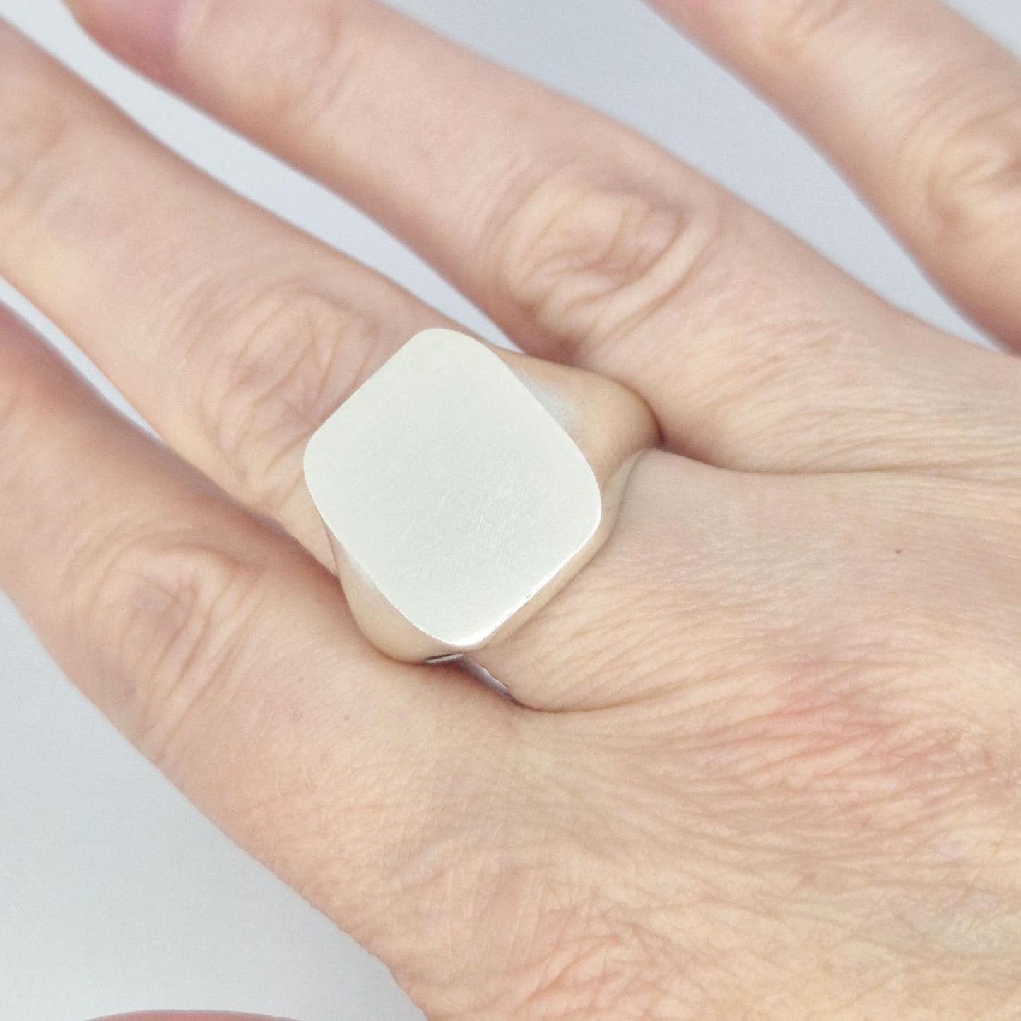 Large silver cushion signet ring worn on hand, showing oversized smooth face and modern minimalist styling.
