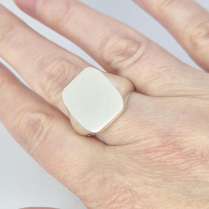 Large silver cushion signet ring worn on hand, showing oversized smooth face and modern minimalist styling.