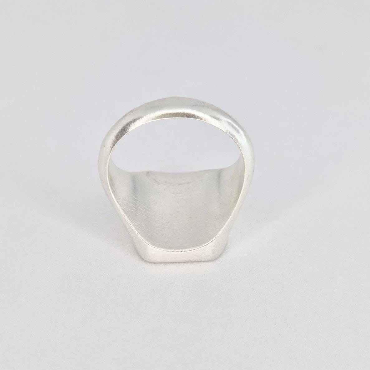 Underside view of a chunky silver cushion signet ring displaying the hollowed interior and smooth band shape.