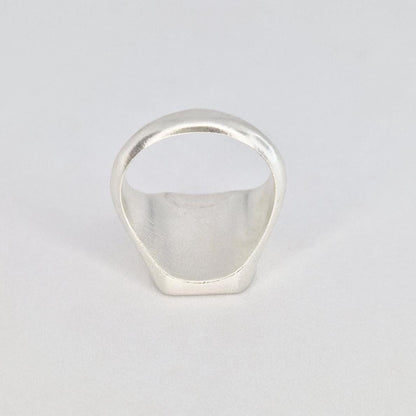 Underside view of a chunky silver cushion signet ring displaying the hollowed interior and smooth band shape.