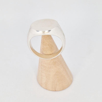 Heavy signet ring on wooden cone display, thick band and flat round face