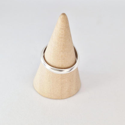 Sterling silver cushion signet ring on wooden cone display, minimalist polished band profile view