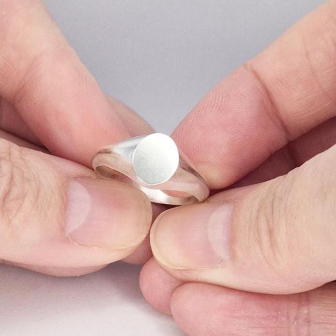 Hands holding a small oval signet ring, demonstrating scale and minimalist design