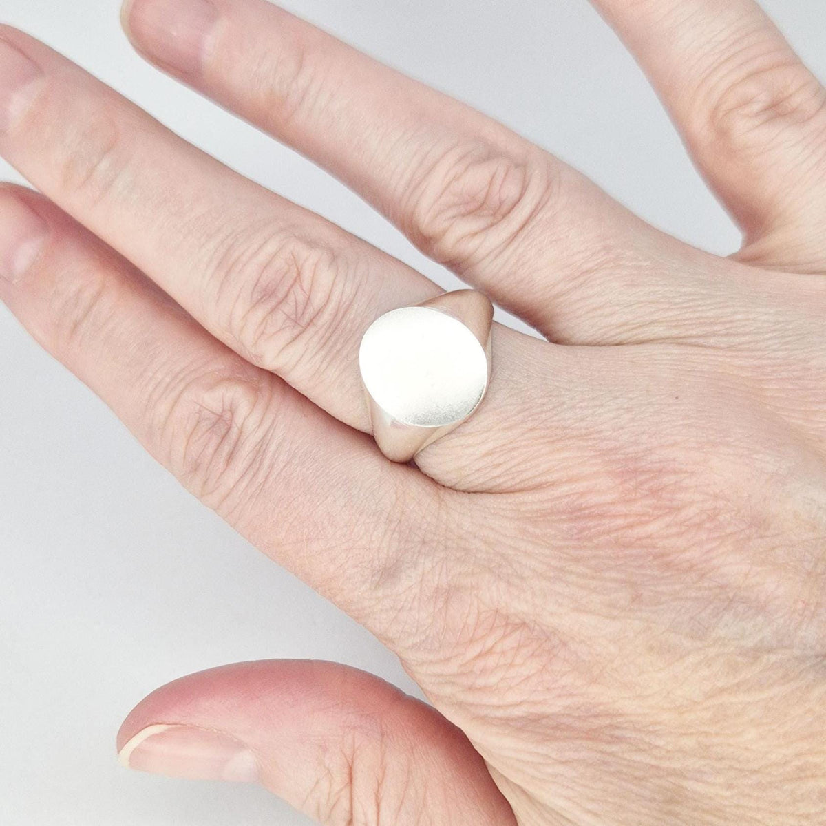 Oval silver signet ring worn on finger, minimalist design with matte face and soft tapered shoulders