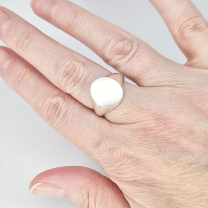Oval silver signet ring worn on finger, minimalist design with matte face and soft tapered shoulders