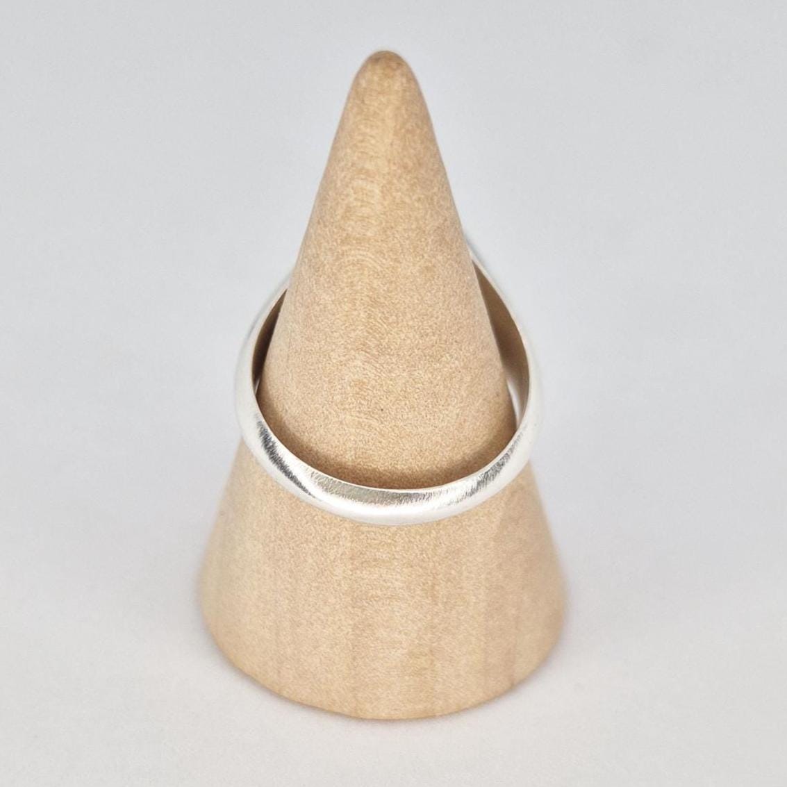 Silver signet ring displayed on wooden cone stand showing band shape from behind