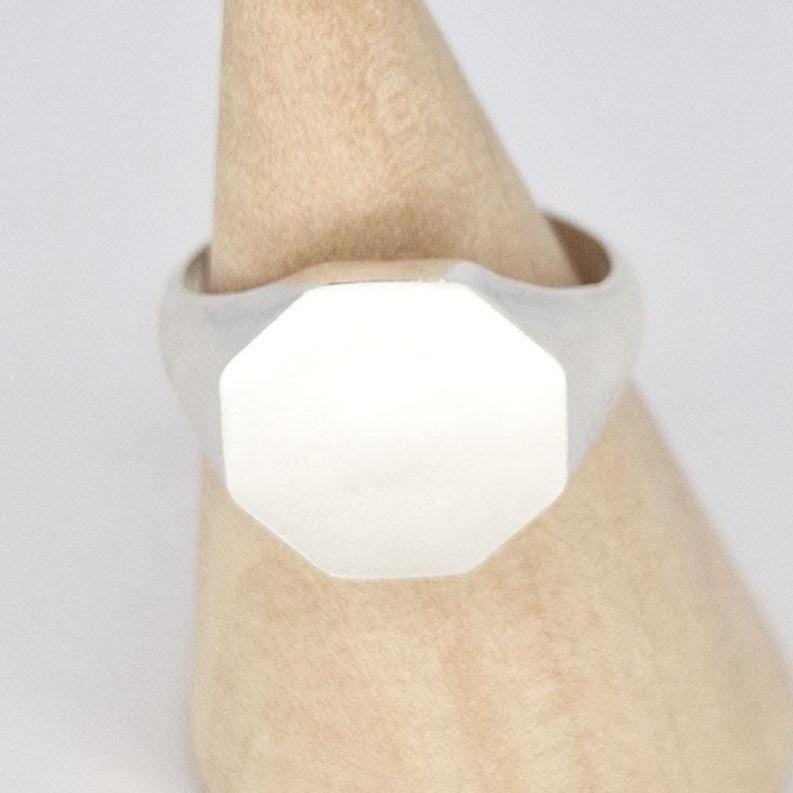 Close-up of octagon signet ring on wooden cone stand showing smooth matte surface and crisp edges