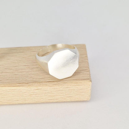 Octagon signet ring displayed on wooden block showing angled face and satin finish