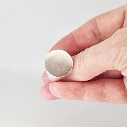 Round signet ring held at slight angle, highlighting brushed satin texture across flat circular face.