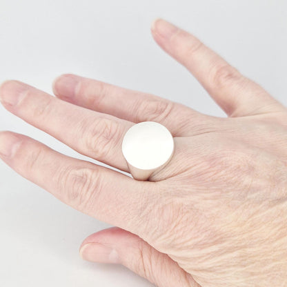 Minimalist round signet ring worn on finger, featuring a large flat circular face in matte silver finish.