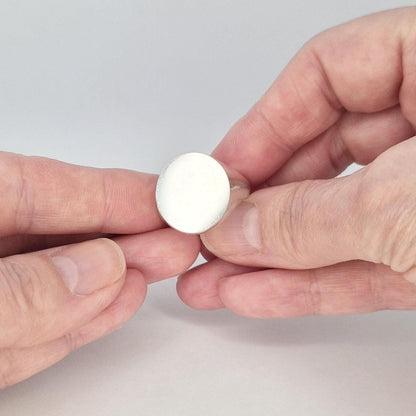 Close-up of round signet ring held between fingers, showing smooth flat 18mm circular face in satin silver.