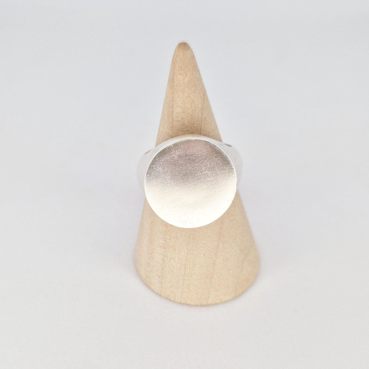 Front-facing view of heavy round signet ring on cone stand, emphasizing bold flat circular face.