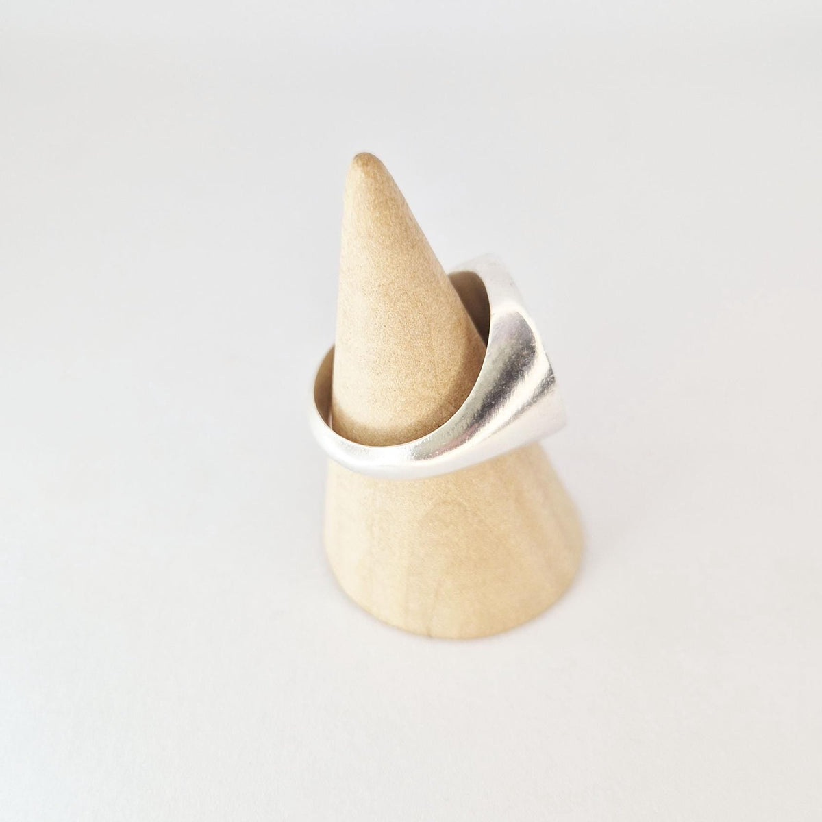 Angled view of signet ring on wooden cone stand, showing smooth taper from band to wide circular face.