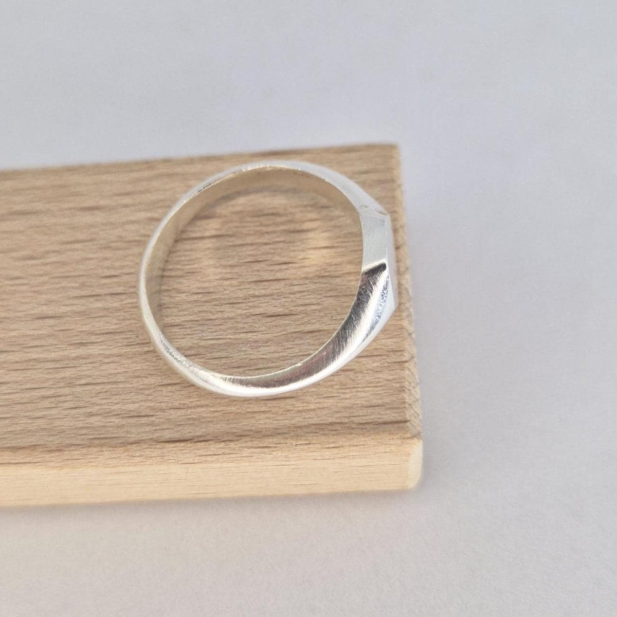 Minimalist hexagon signet ring in silver resting on wood block, smooth tapered band and flat geometric face