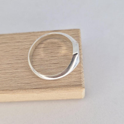 Minimalist hexagon signet ring in silver resting on wood block, smooth tapered band and flat geometric face