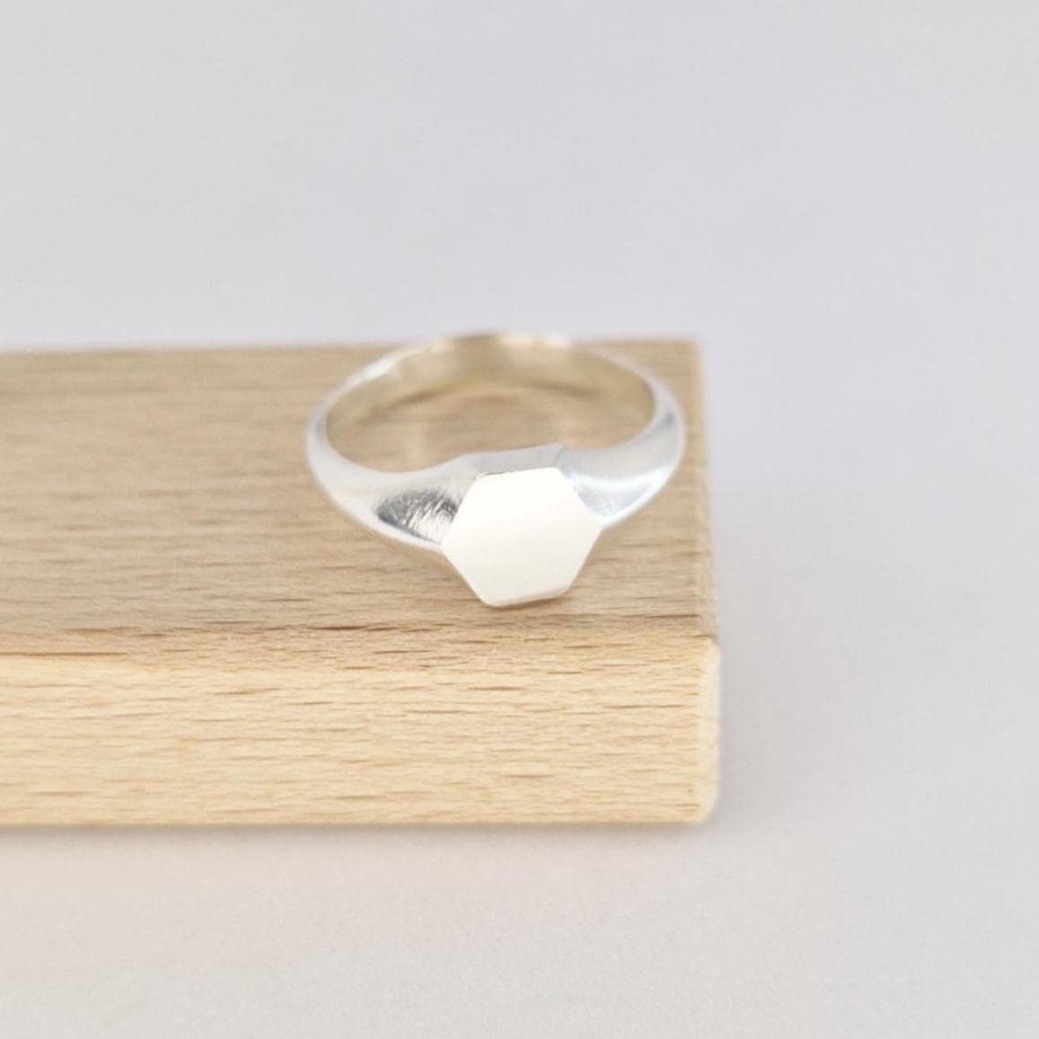 Hexagon signet ring in sterling silver displayed on wooden stand, modern geometric face design