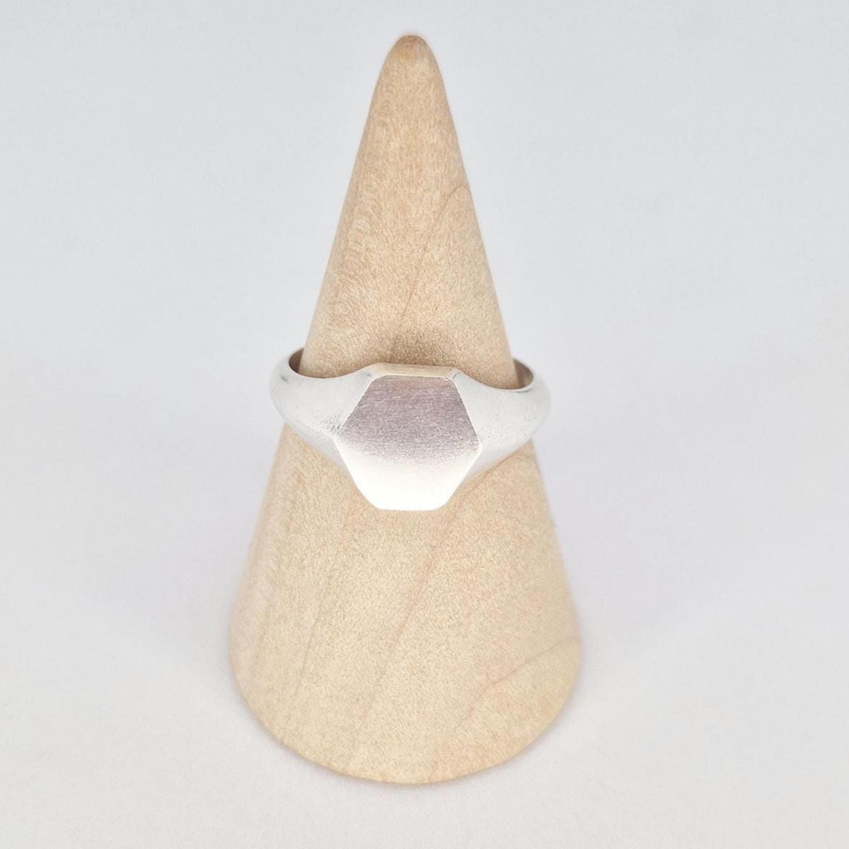 Front view of sterling silver hexagon signet ring on wooden cone, satin face with polished edges