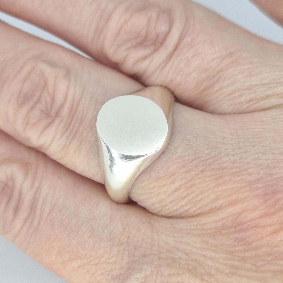 Handmade oval signet ring worn on finger, featuring a smooth satin-finished oval face and polished silver tapered shoulders.