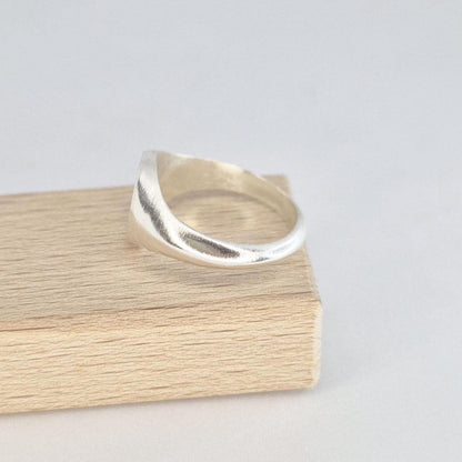 Side profile of a minimalist silver oval signet ring resting on a wooden display block, highlighting the tapered band design.