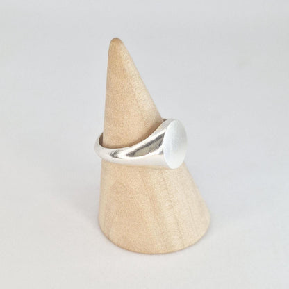Side angle of a minimalist sterling silver oval signet ring on a wooden cone display, showing the smooth tapered shoulders.