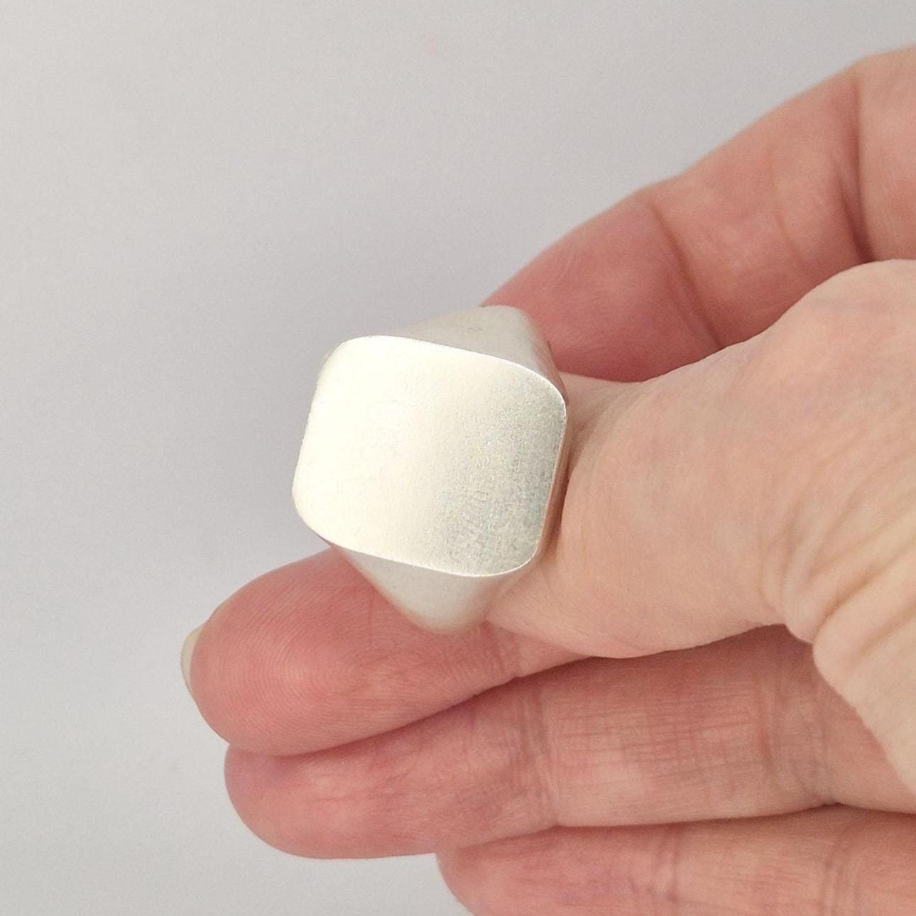 Close-up angled view of a minimalist cushion signet ring with satin finish and tapered shoulders in solid silver.