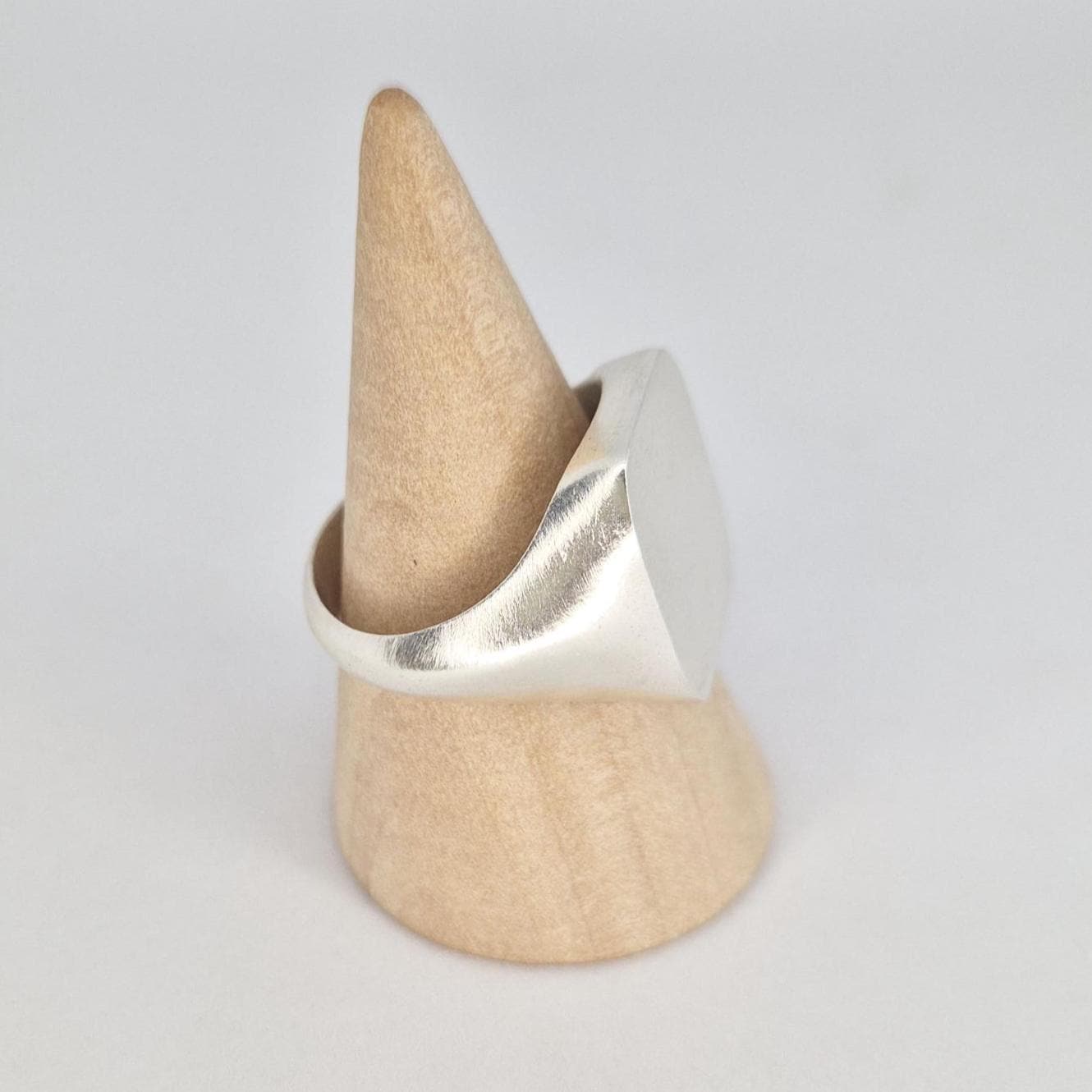 Angled side view of a minimalist silver cushion signet ring on wooden display cone with satin brushed face and polished shoulders.