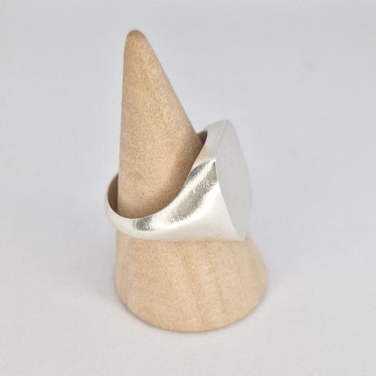 Angled side view of a minimalist silver cushion signet ring on wooden display cone with satin brushed face and polished shoulders.