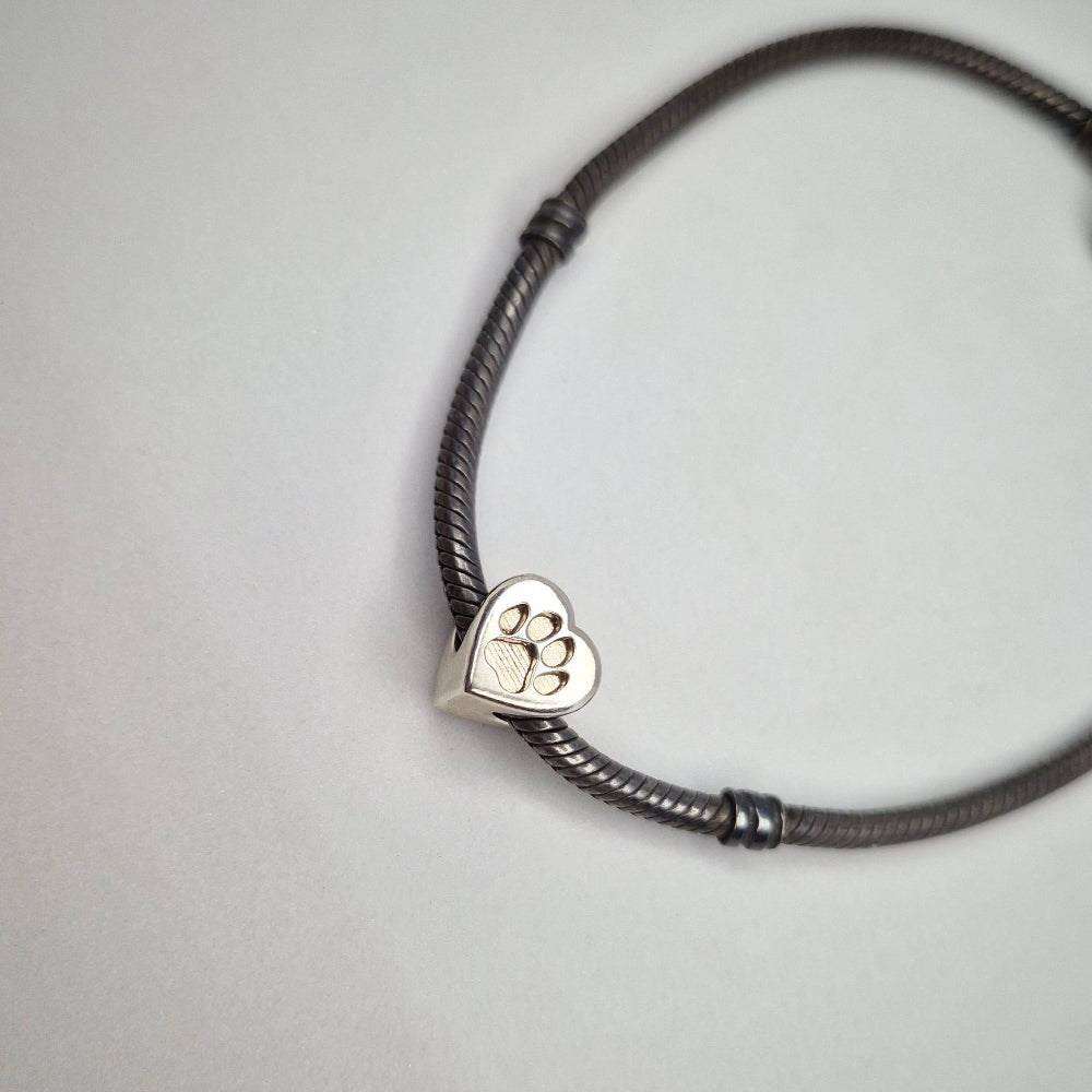 A bracelet bead in silver on a bracelet against a white background. Featuring a recessed paw print for resin casting.