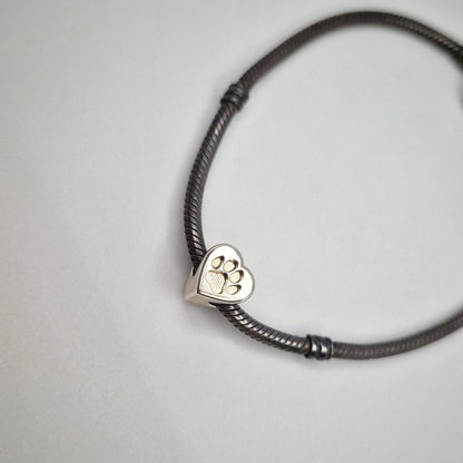 A bracelet bead in silver on a bracelet against a white background. Featuring a recessed paw print for resin casting.
