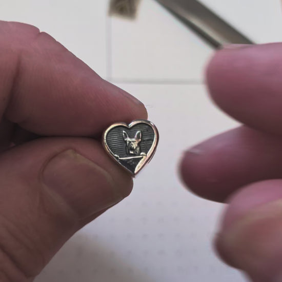 A silver bead featuring a dog on one side and a paw print on the other.