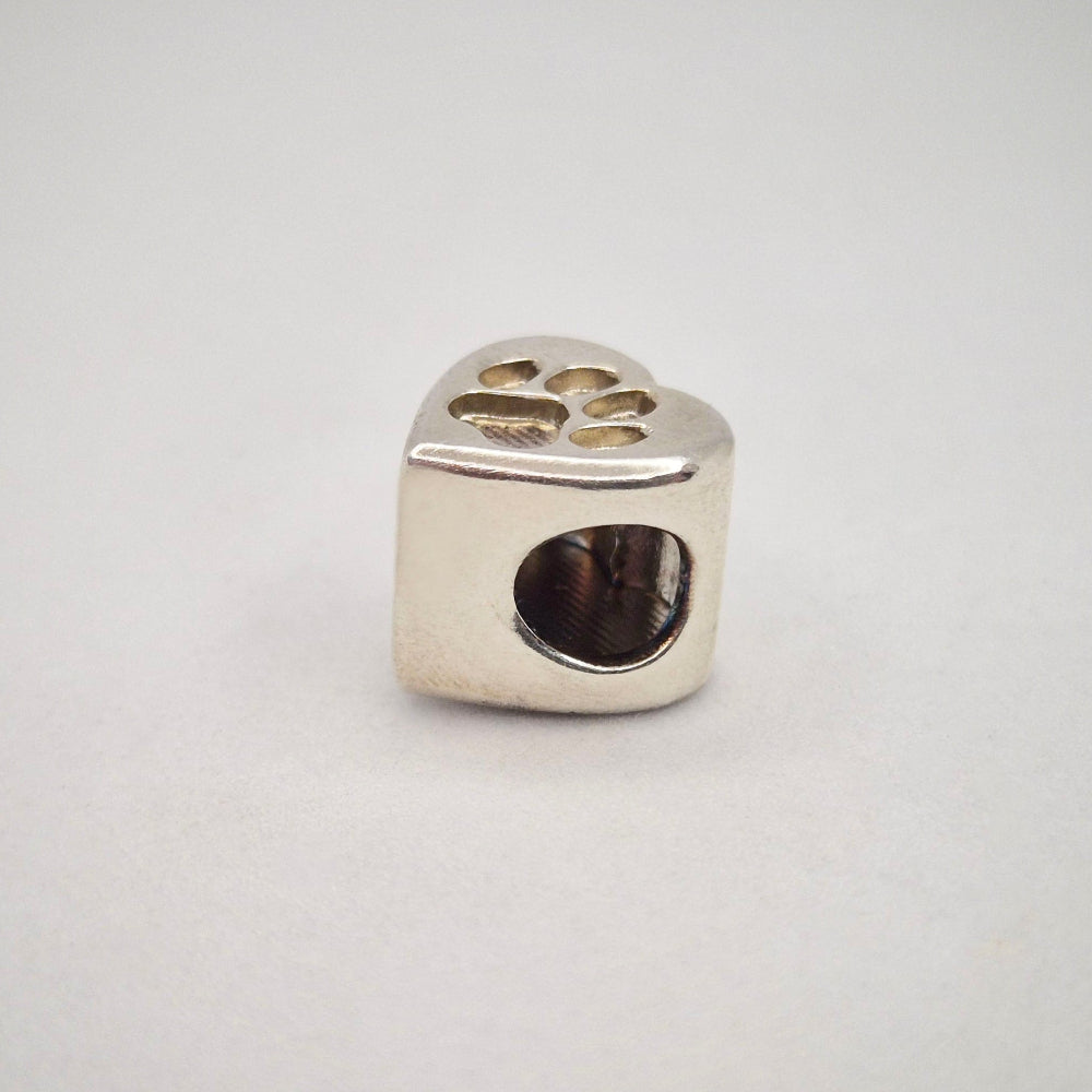 A silver bracelet bead featuring a paw print recess.