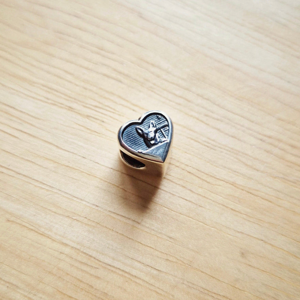 A silver dog bracelet bead against a wooden background.