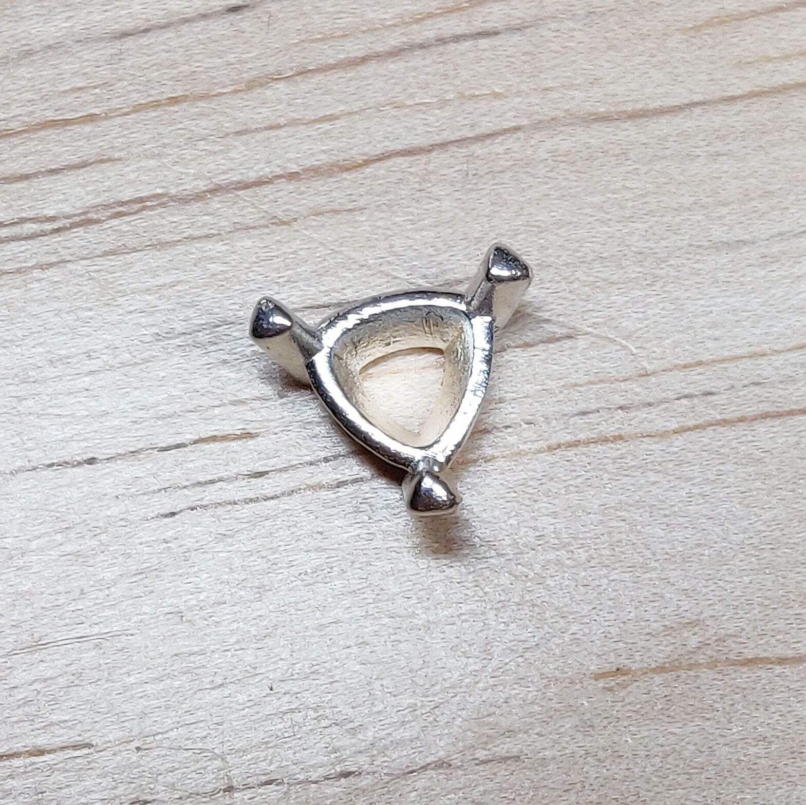 Top view of a silver trillion prong setting on a wooden background.