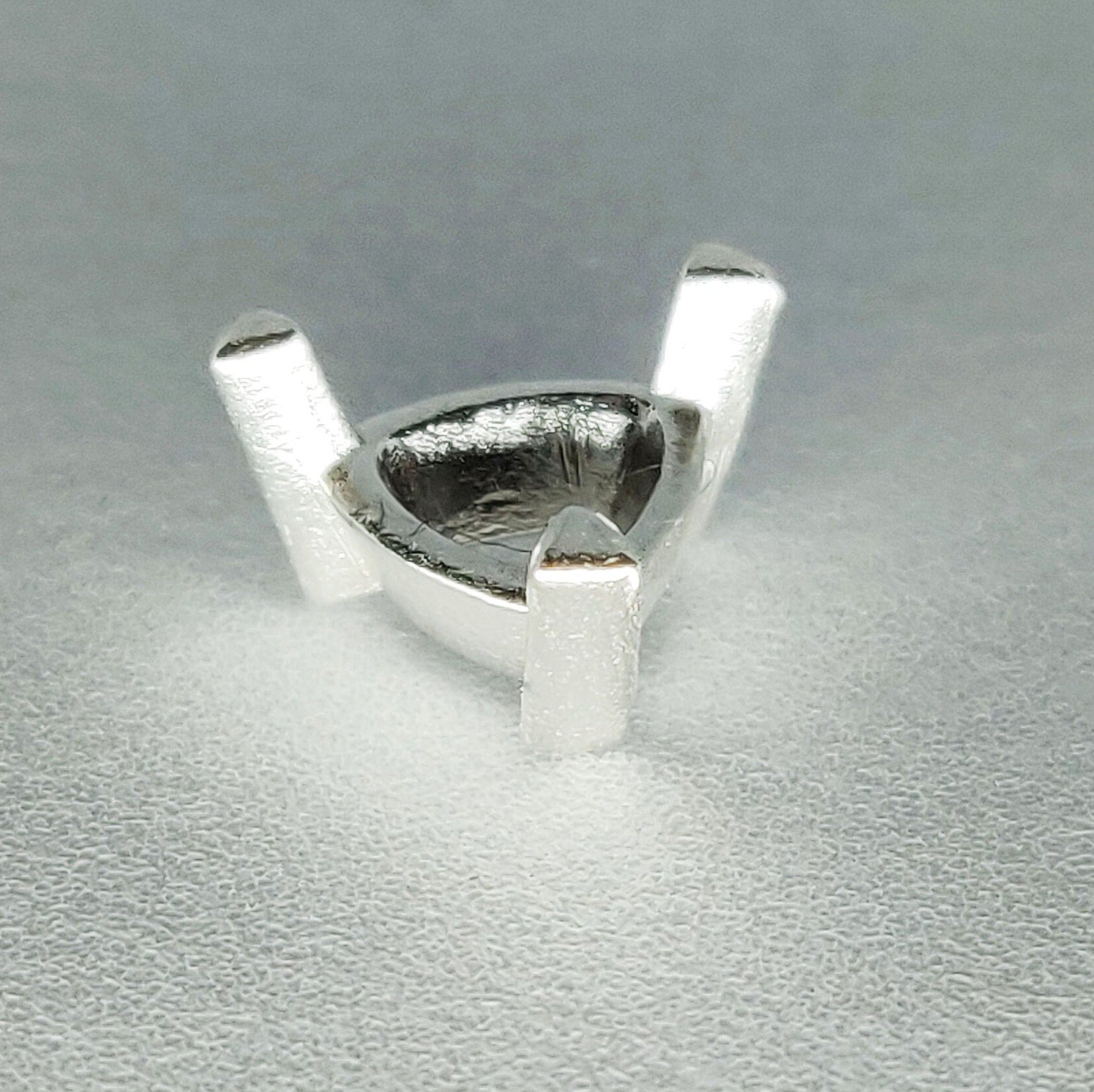 Profile view of a silver trillion prong setting on a white background.