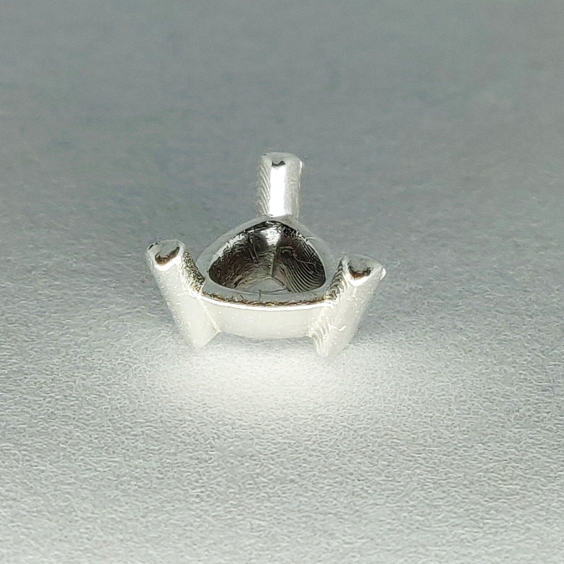 Profile view of a silver trillion prong setting on a white background.